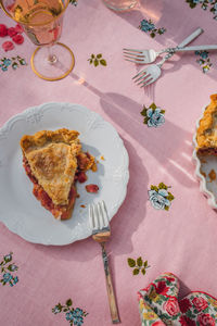 Single slice of rhubarb pie on white plate, pink tablecloth with blue roses, rose wine