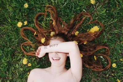 High angle view of shirtless smiling teenage girl covering eyes while lying on grass