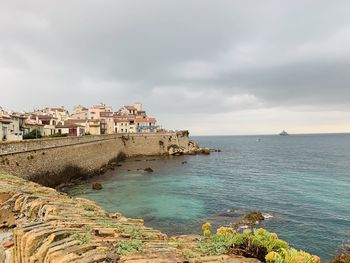 Buildings by sea against cloudy sky