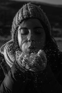 Close-up of teenage girl wearing warm clothing blowing snow