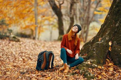 Young woman sitting on tree during autumn