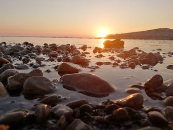 Rocks on beach against sky during sunset