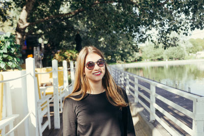 Portrait of smiling mid adult woman wearing sunglasses standing on footbridge