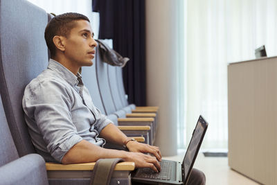 Serious young student using laptop while sitting at lecture hall in university