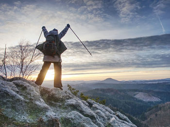 Woman reached mount peak. girl wearing backpack using trekking sticks, enjoying cloudy daybreak