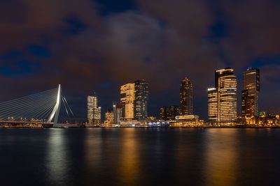 Illuminated city by river against sky at night