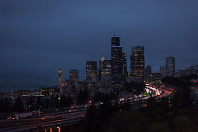 Light trails on road amidst buildings against sky at night