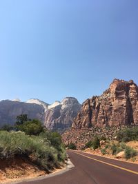 Road leading towards mountains against clear sky