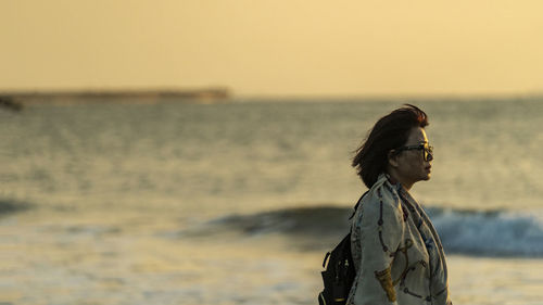 Side view of person looking at sea against sky during sunset