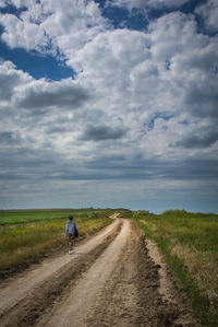 Rear view of man cycling on road against sky