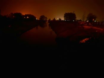 Reflection of silhouette trees on illuminated orange sky