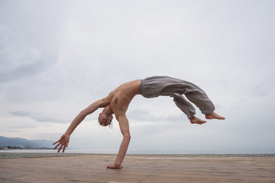 Low angle view of woman exercising at beach against clear sky