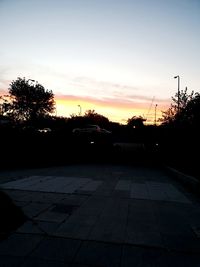 Silhouette trees by footpath against sky at sunset