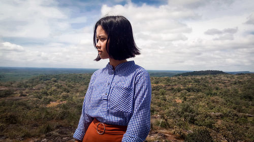 Thoughtful woman with landscape in background against cloudy sky