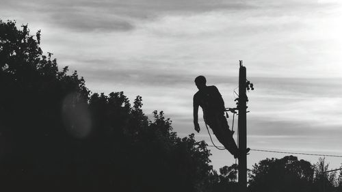 Low angle view of silhouette man standing on telephone pole against sky