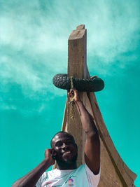 Low angle view of man holding sculpture against blue sky