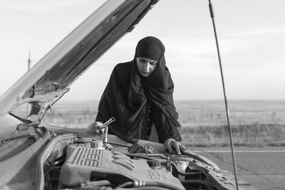 Tired woman standing by breakdown car against sky