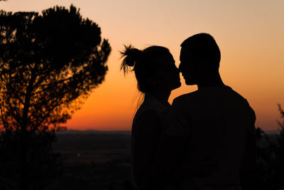 Close-up of couple standing against orange sky