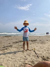 Rear view of boy with arms outstretched standing at beach against sky