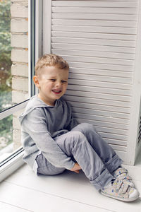 Portrait of a child boy four years old sitting on a wooden floor in next to a large window