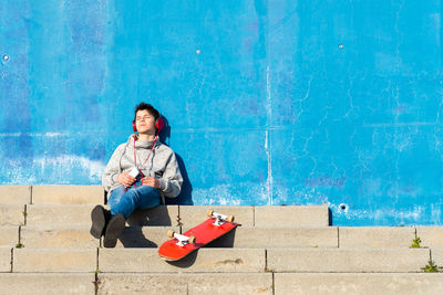 Teenager with headphones listening music while sitting on staircase.