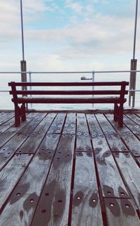 Empty bench on pier against sky