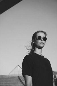 Portrait of young woman wearing sunglasses standing at beach against sky