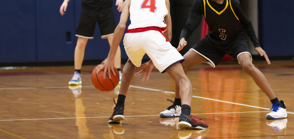 Basketball point guard dribbling the basketball between his legs while being defended during a game.