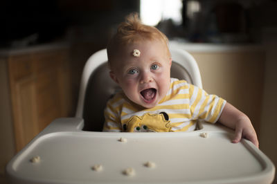 Portrait of cute baby boy playing with breakfast cereal while sitting on high chair