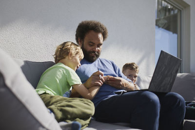 Father sitting with sons on deck and working on laptop