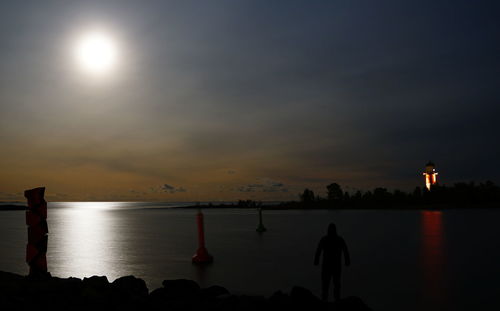 Silhouette people standing by sea against sky during sunset