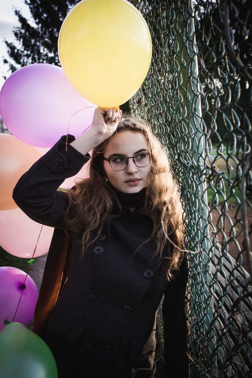 one person, real people, lifestyles, balloon, young women, leisure activity, looking at camera, portrait, young adult, front view, women, standing, fence, beauty, hair, casual clothing, barrier, hairstyle, beautiful woman, outdoors, teenager