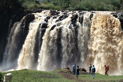 People standing against waterfall on field