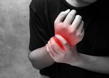 Midsection of man suffering wrist pain against wall