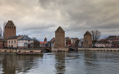 View of buildings by river against cloudy sky