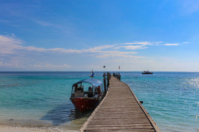 Boat moored by jetty over sea against blue sky