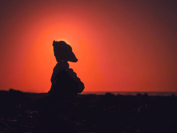 Silhouette person standing on rock during sunset