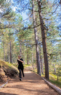 Rear view of man walking on road amidst trees in forest