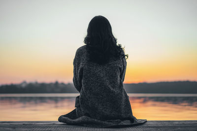 Rear view of woman standing by lake against sky during sunset