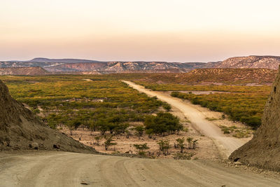 Dirt road amidst landscape against sky during sunset