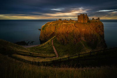 Dunnottar castle by sea against sky during sunset