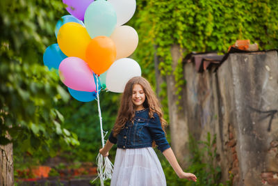 Smiling girl holding balloon standing outdoors