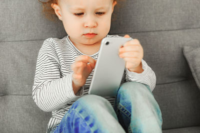 Little curly girl using mobile phone while sitting on sofa