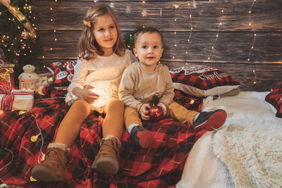 Sister and little baby brother in living room decorated by christmas tree and present gift box