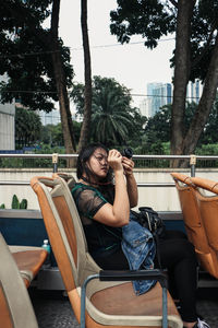 Side view of young woman photographing while sitting on chair