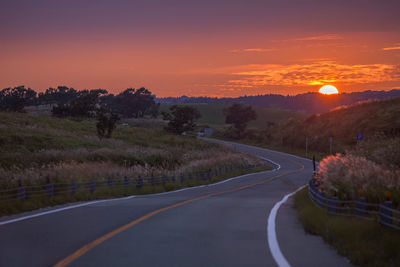 Road amidst trees against sky during sunset