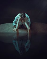 Cropped hand holding woman face through water in dark room