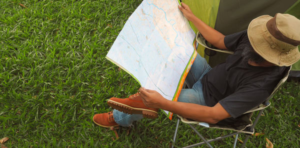 High angle view of man reading map while sitting on chair at campsite