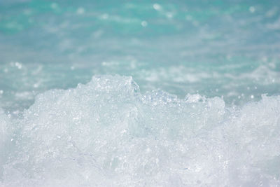 The sea wave breaks on the shore and causes water and white airy foam to splash.