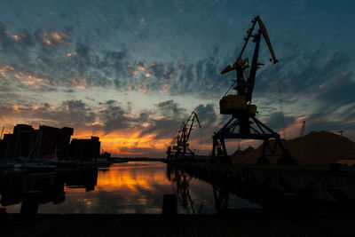 Silhouette cranes against sky at sunset